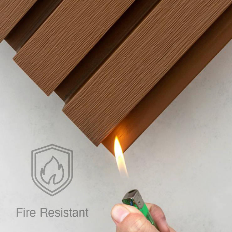 A hand holds a lit lighter to brown Landmark Decor Teak Color Exterior WPC Panel; a “Fire Resistant” icon in the corner highlights its fire and weather resistance, making it ideal for outdoor wall decoration.
