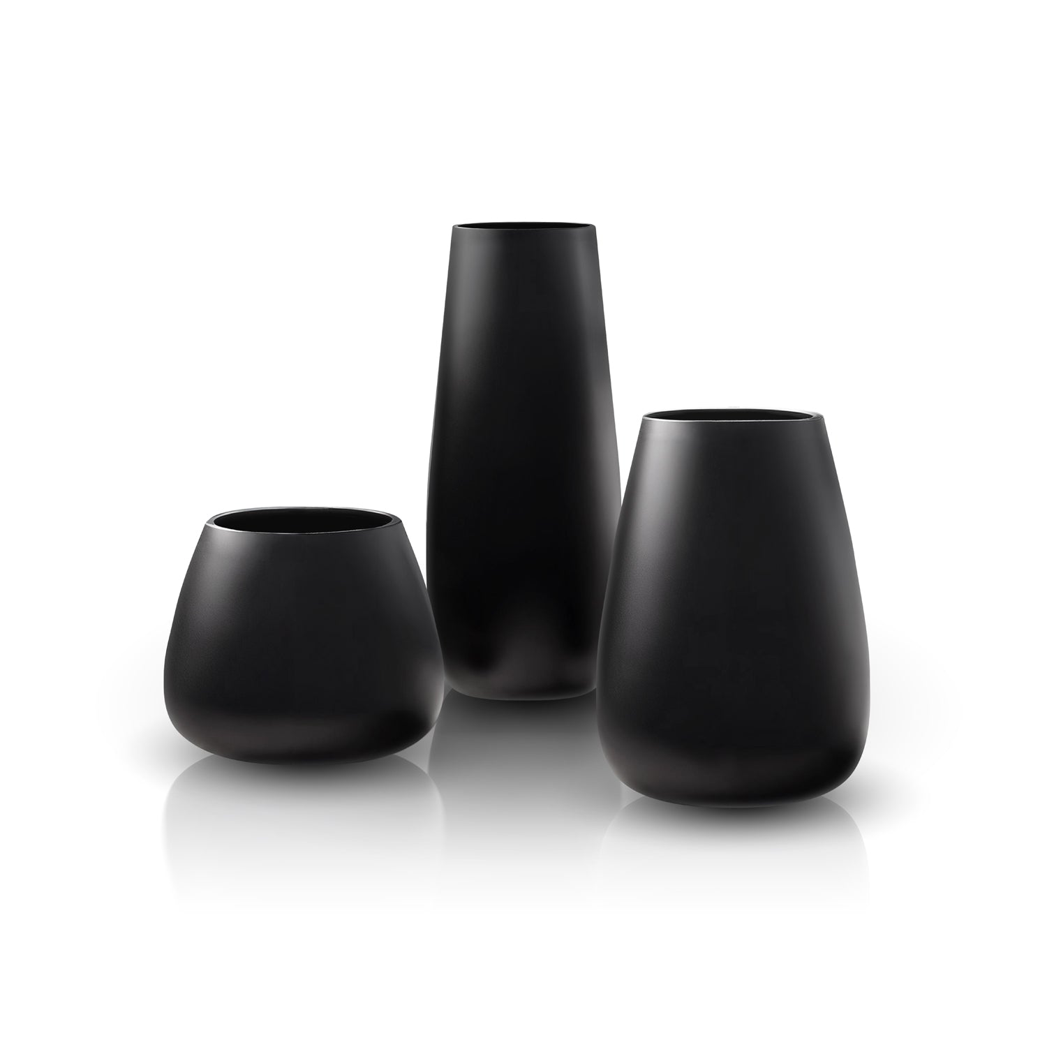 The Ombra di Obsidiana Planter by Landmark Decor features three handmade matte black vases of varying heights and shapes. Their minimalist design is enhanced as they sit on a reflective white surface, creating gentle reflections below.